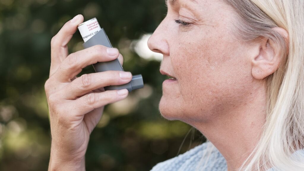 A woman using an inhaler outdoors.